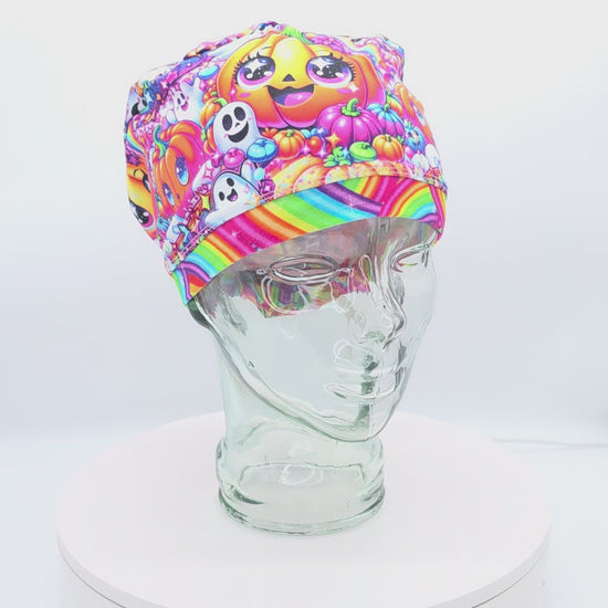 360-degree rotating video display of a full-coverage medical scrub cap featuring a colorful rainbow pumpkin pattern with cute jack-o'-lantern faces on a glass mannequin head.